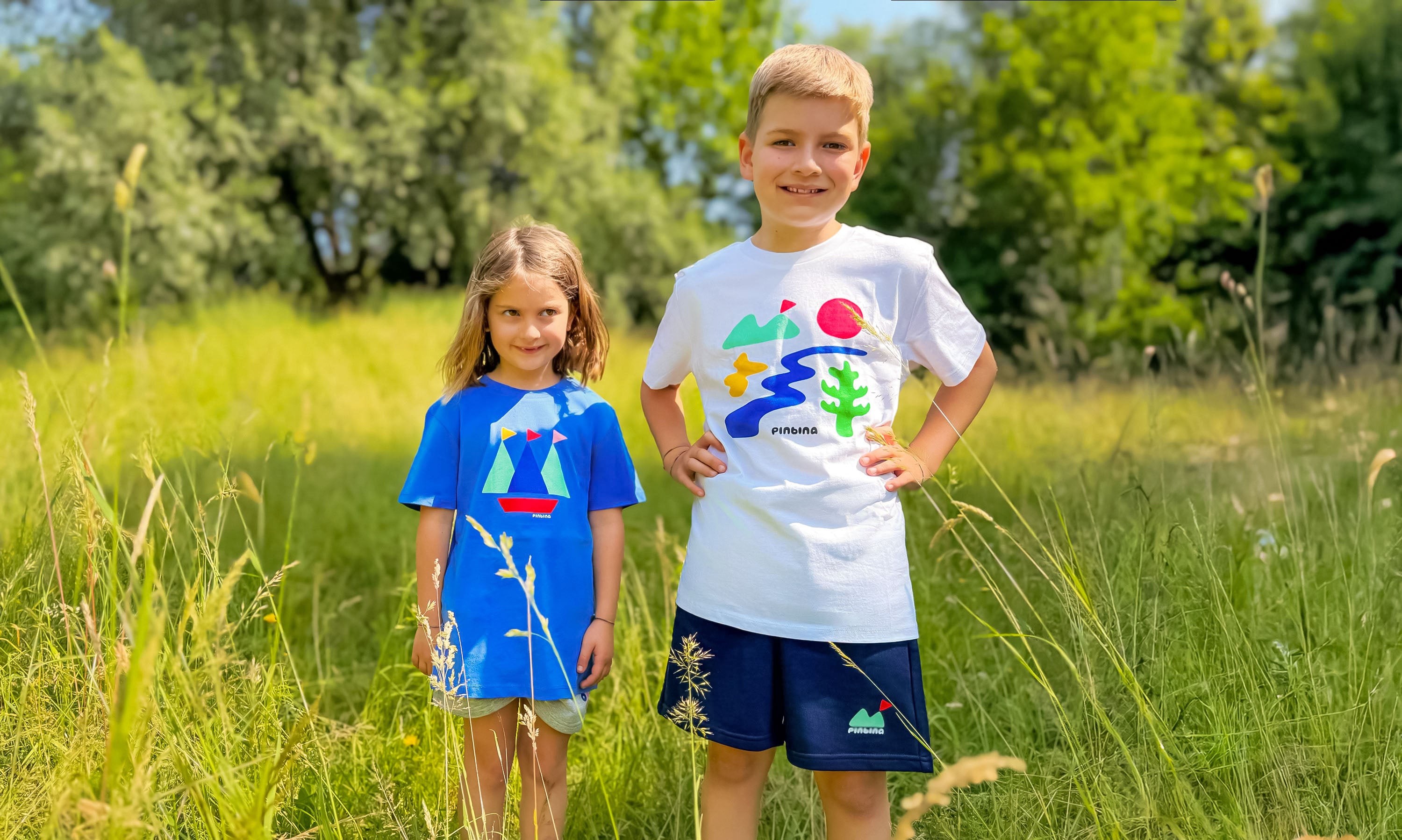 Two children standing in a grassy field wearing colorful shirts with nature-themed designs.